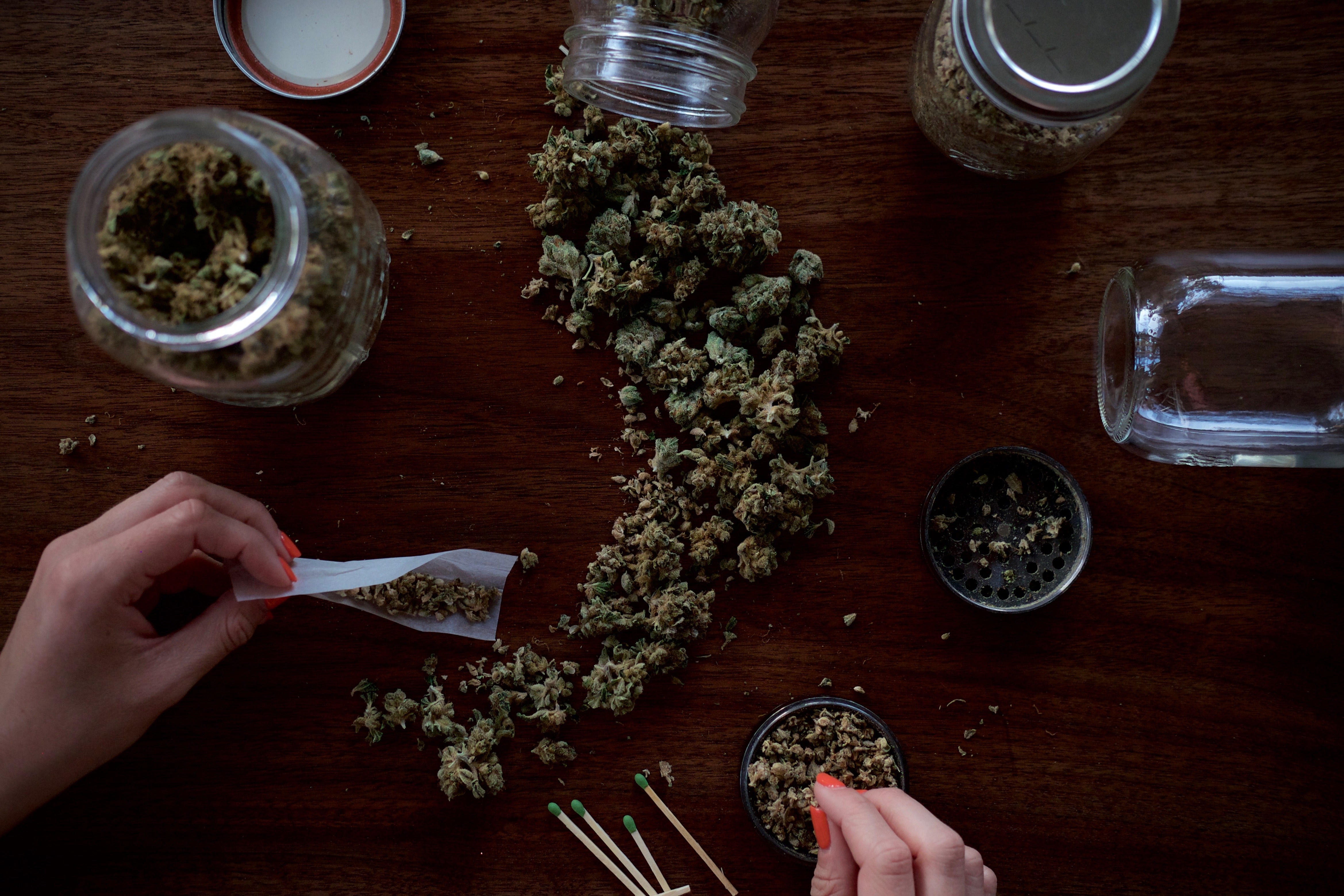 human hands above table with spilled cannabis jar, rolling joints with papers